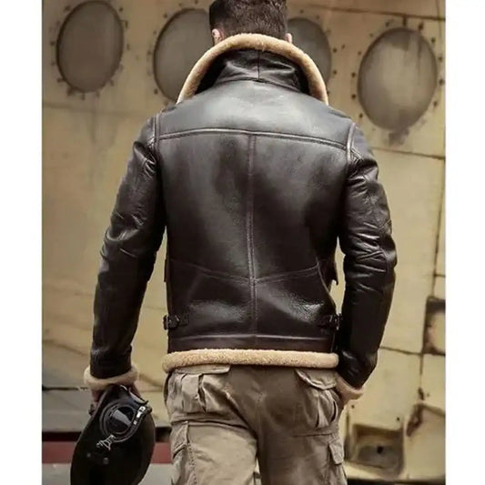 A man viewed from behind wearing a dark brown leather aviator jacket with a beige shearling lining, paired with khaki cargo pants and holding a black helmet, set against a vintage aircraft fuselage background.