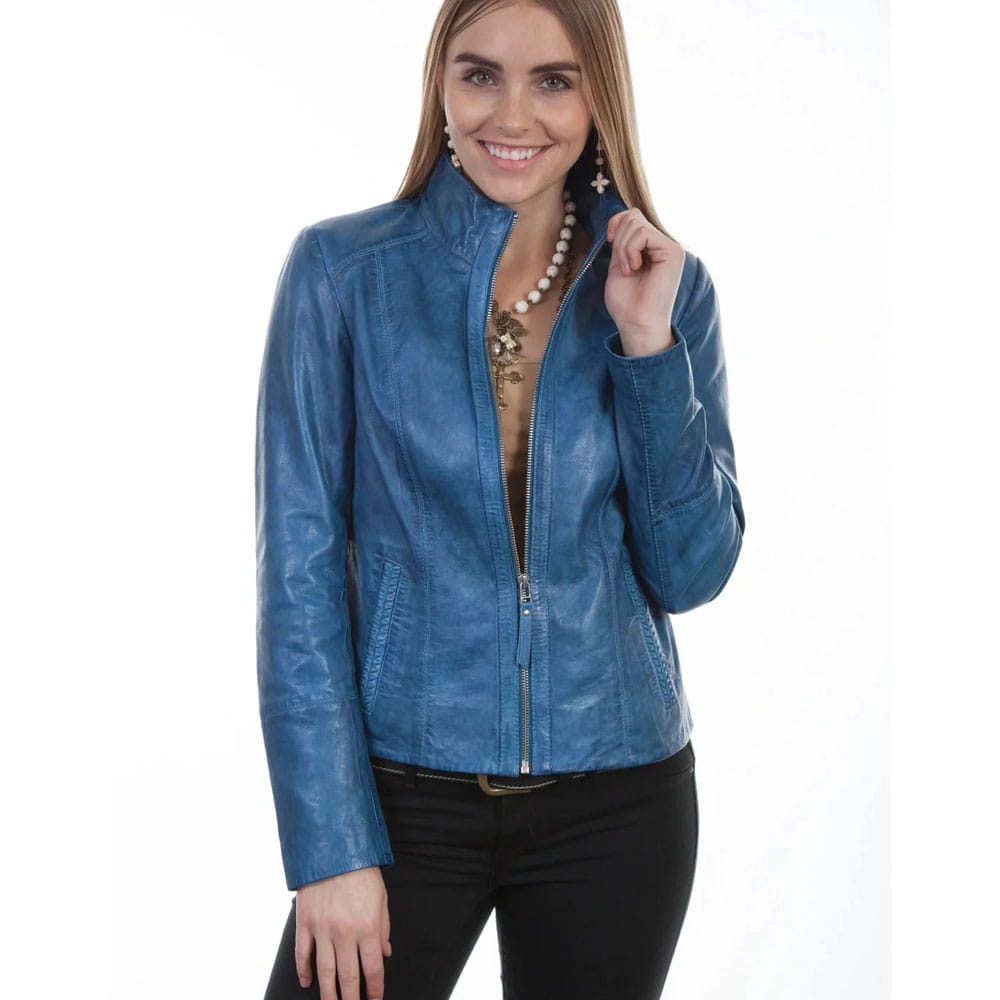A woman wearing a blue faux-leather zip-up jacket, styled with a gold necklace and earrings, paired with black pants, against a plain white background.