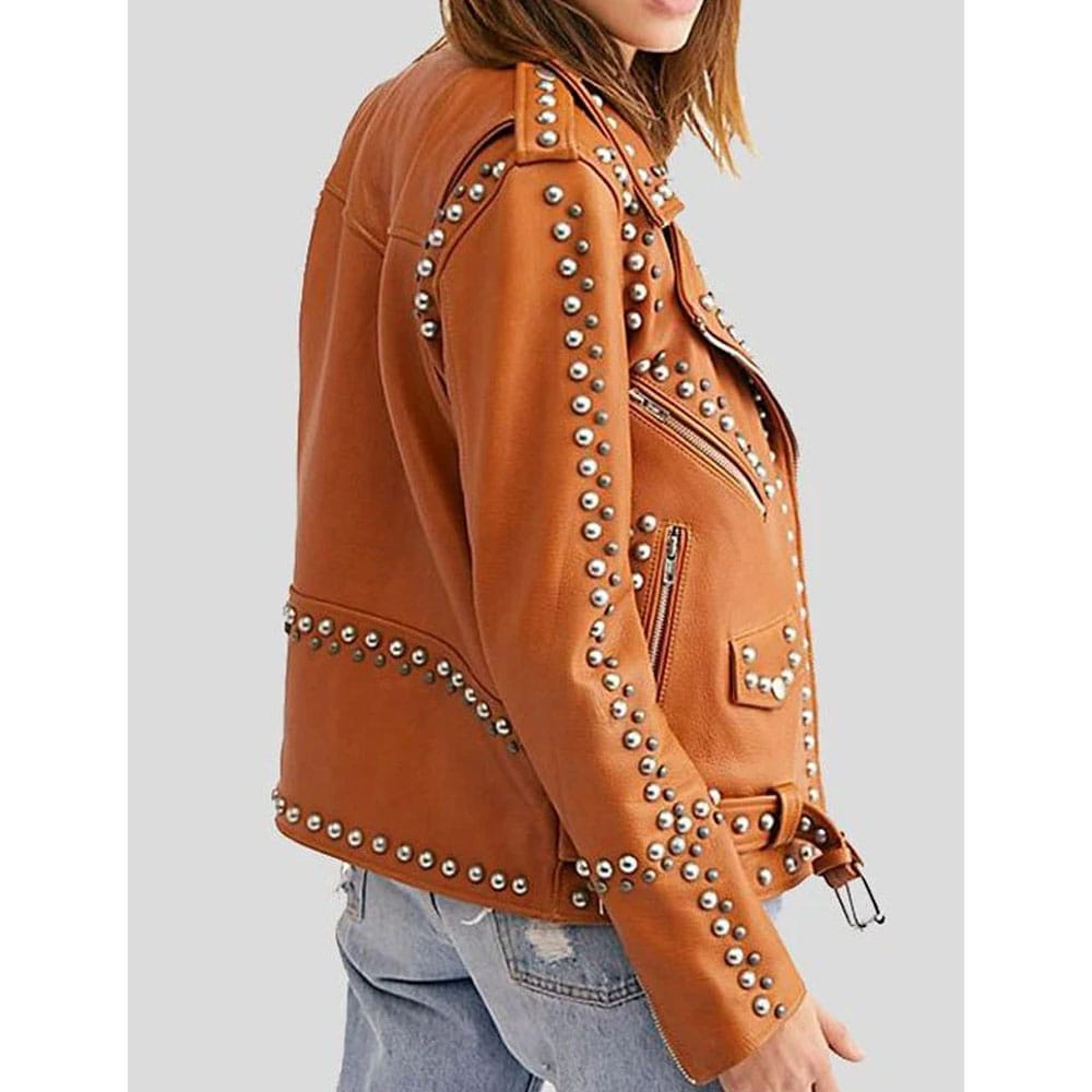 A woman wearing a tan-brown faux leather motorcycle jacket decorated with silver studs, shown from a side profile against a light gray background.