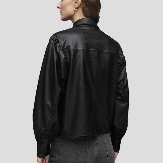A woman shown from the back wearing a black leather jacket with gathered sleeves and dark gray jeans, set against a solid light gray background.