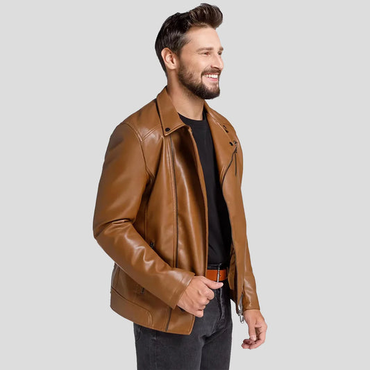 A man wearing a brown faux leather motorcycle jacket over a black t-shirt and dark jeans, standing against a solid light gray background.