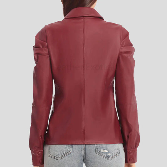 A woman viewed from the back wearing a fitted burgundy faux leather jacket with puffed sleeves and light-wash distressed jeans, against a plain light gray background.