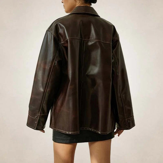 A person shown from the back wearing an oversized dark brown faux-leather jacket over a black mini skirt, photographed against a plain light beige studio background.