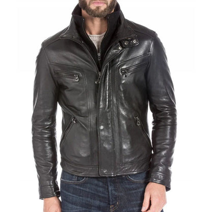A man wearing a black leather motorcycle jacket with a high collar, front zipper, and zippered chest pockets, paired with blue jeans against a white background.