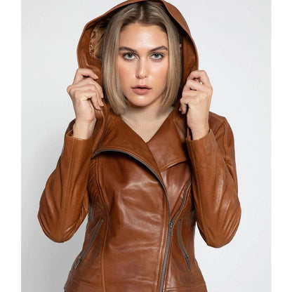 A woman wearing a brown faux-leather hooded jacket with an asymmetrical zipper, holding the hood up against a light gray studio background.