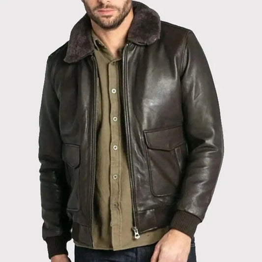 A man wearing a dark brown leather aviator-style jacket with a dark brown shearling collar, layered over an olive green button-down shirt and blue jeans, against a light gray background.