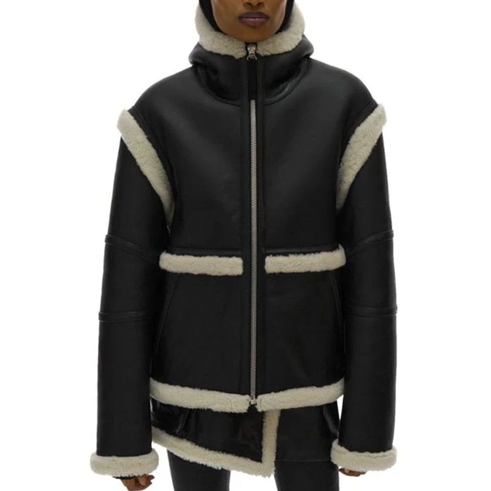 A black faux-leather hooded jacket with cream-colored shearling-style trim, featuring a full front zipper, high collar, and horizontal trim details, shown on a model against a white background.