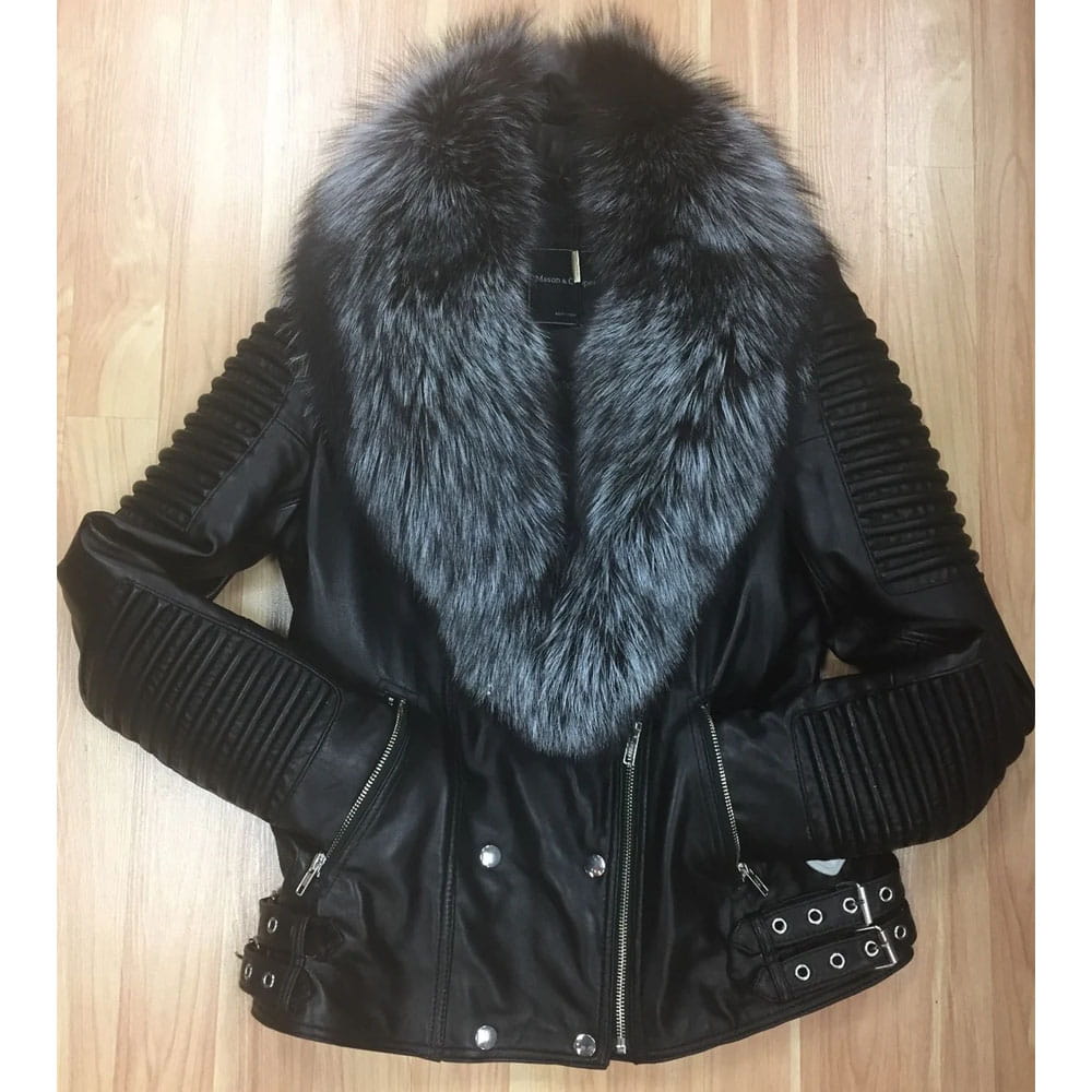 A black faux-leather motorcycle jacket with a large gray and black fur collar, ribbed sleeves, and silver hardware, laid flat on a light wood floor.