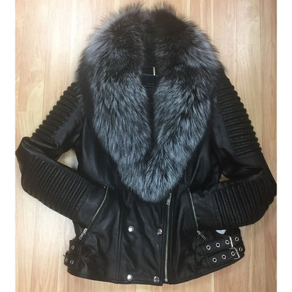 A black faux-leather motorcycle jacket with a large gray and black fur collar, ribbed sleeves, and silver hardware, laid flat on a light wood floor.