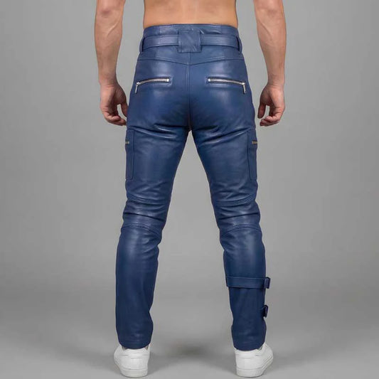 Rear view of a man wearing blue leather pants with zippered cargo pockets and a belt, paired with white sneakers, against a gray studio background.