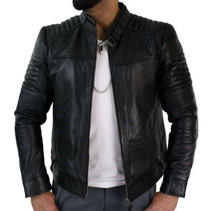 A man wearing a black leather biker jacket with ribbed shoulders and sleeves, styled over a white t-shirt and gray pants against a white background.