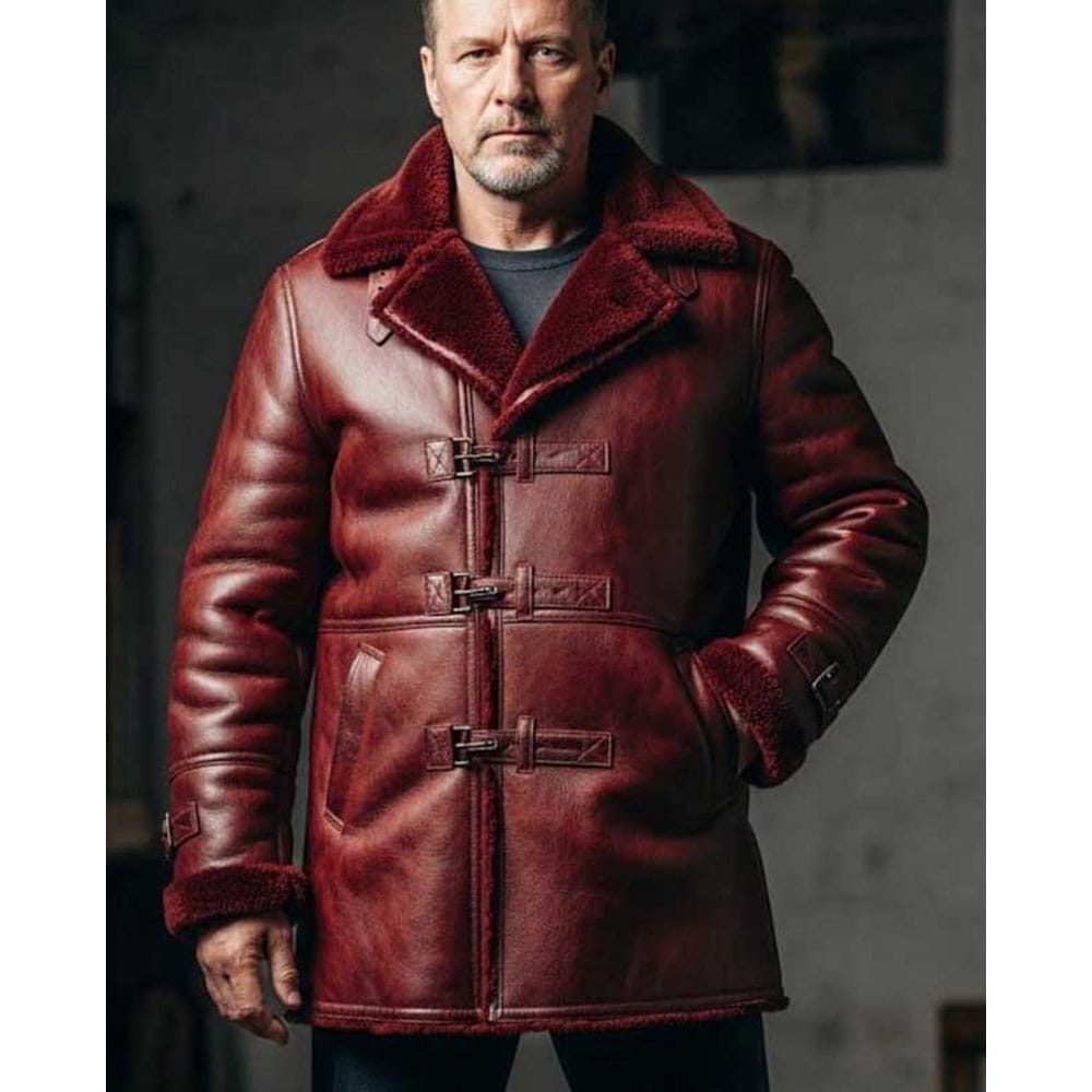 A man wearing a dark red leather duffle coat with a plush brown shearling collar and cuffs, standing against a dark gray background.