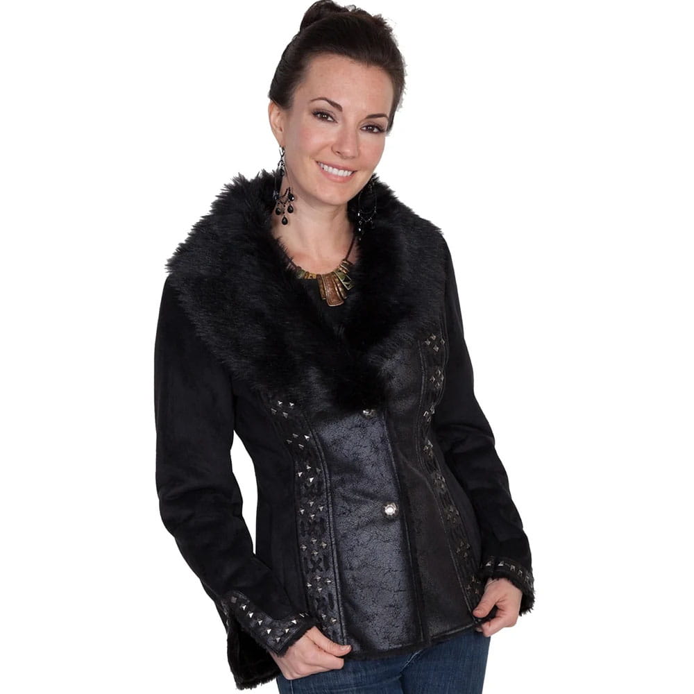 A woman wearing a black faux-fur and textured leather jacket with silver studs, paired with blue jeans, against a plain white background.
