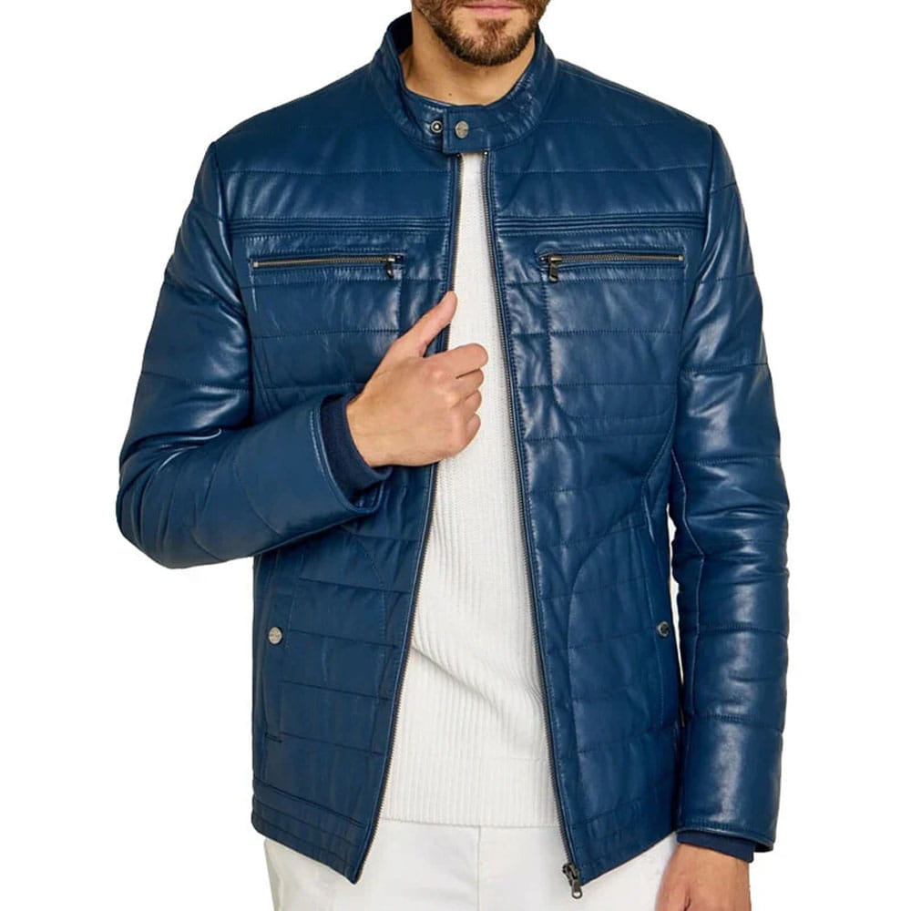 A man wearing a navy blue quilted faux-leather jacket over a white ribbed sweater and white pants, shown from the waist up against a plain white background.