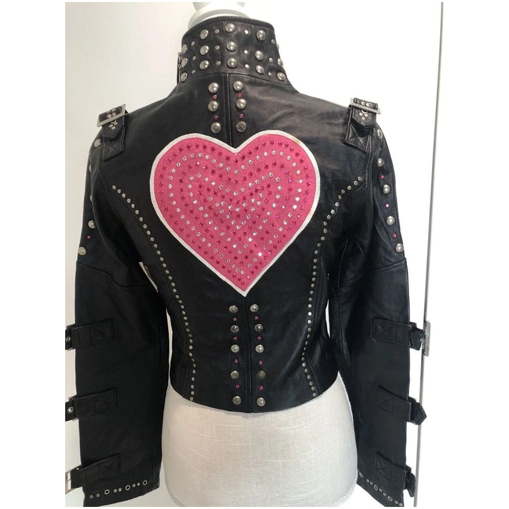 Black leather jacket with silver studs and a large pink heart embellishment on the back, displayed on a mannequin torso.