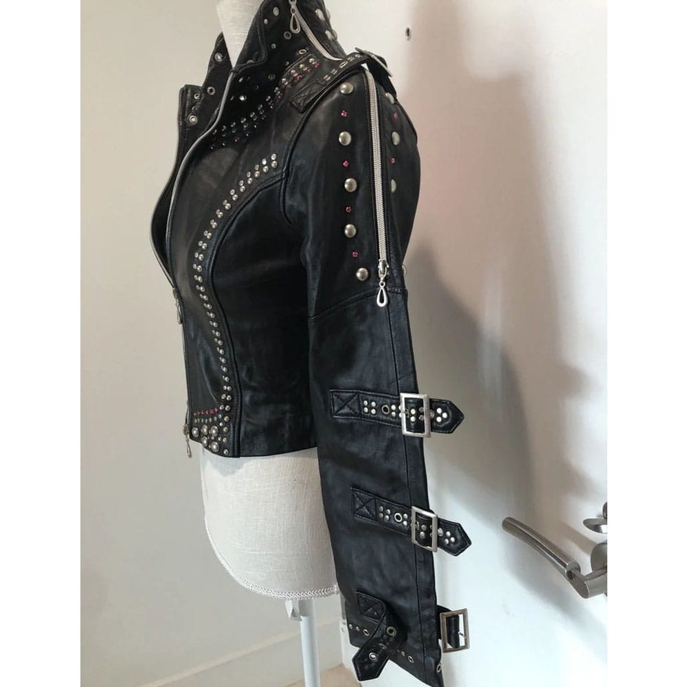 Black leather jacket with silver studs, zippers, and buckle details, displayed on a white dress form mannequin against a white wall.