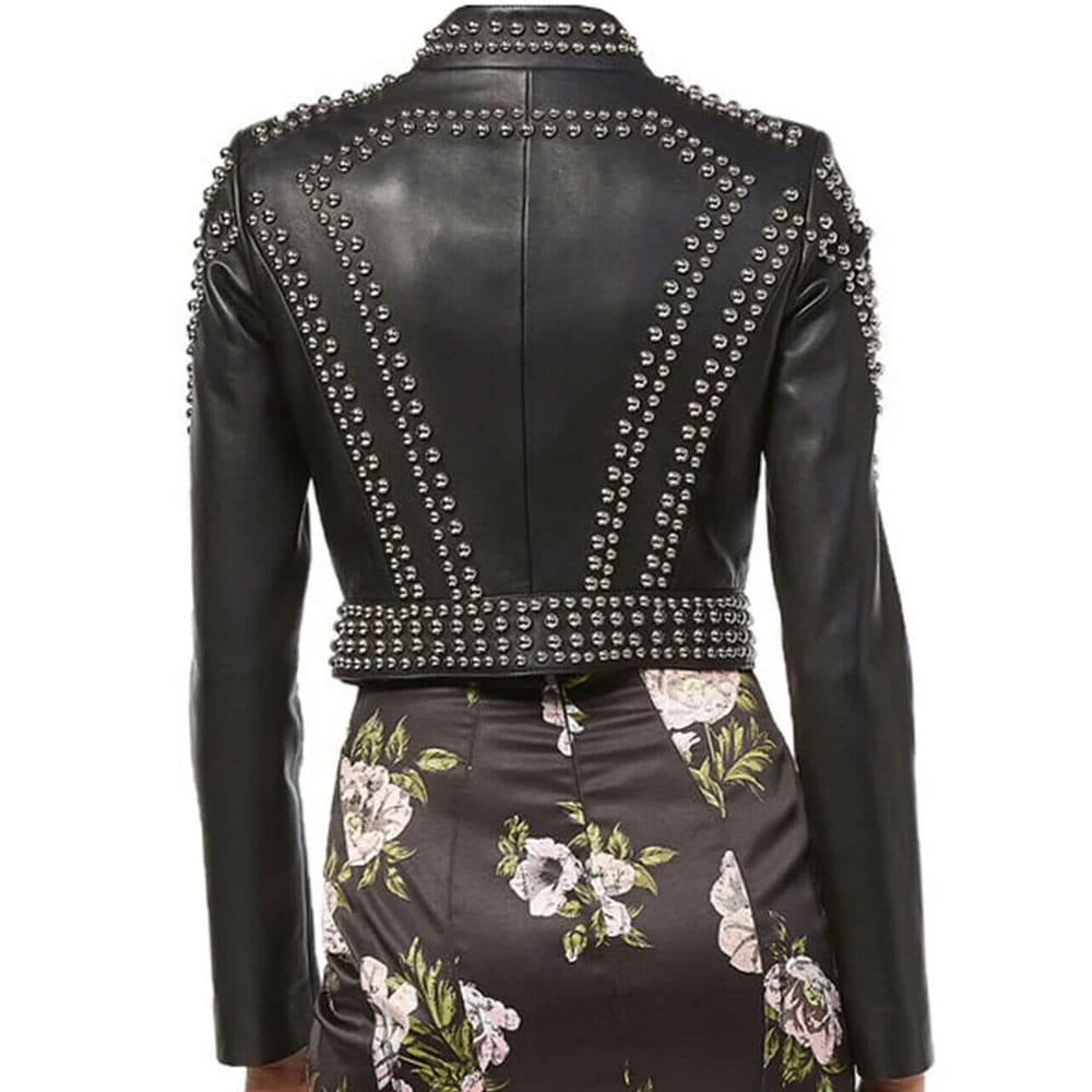 Rear view of a black faux leather jacket with silver studs, worn with a dark floral skirt against a white background.