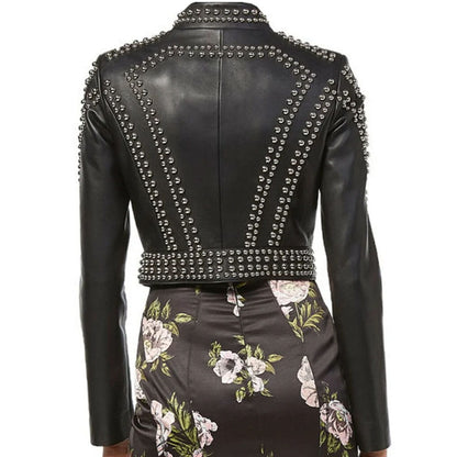 Rear view of a black faux leather jacket with silver studs, worn with a dark floral skirt against a white background.