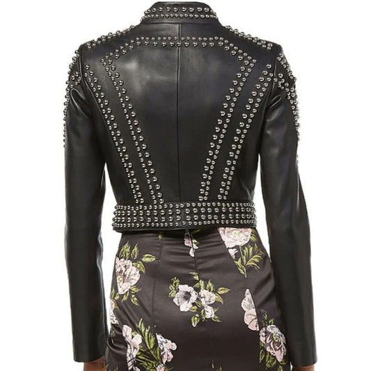 Rear view of a black faux leather jacket with silver studs, worn with a dark floral skirt against a white background.