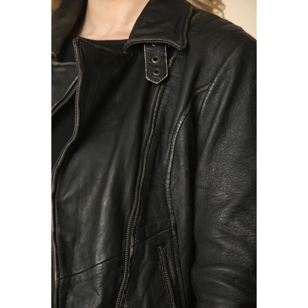 Close-up of a black leather jacket worn by a model, showing the collar, front zipper, and textured leather fabric.