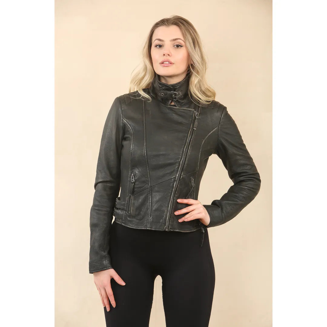 A woman modeling a black faux-leather moto jacket with a high mock neck and asymmetrical zipper, paired with black pants, against a solid beige studio background.