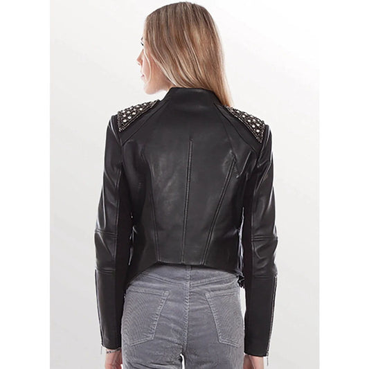 A woman shown from the back wearing a black leather moto jacket with silver studded shoulder details, paired with gray jeans, against a plain white studio background.