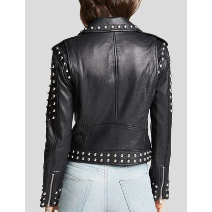 A black leather moto jacket with silver studs and zippers, shown from the back on a model wearing light blue jeans against a gray background.