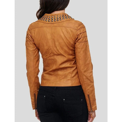 A woman viewed from the back wearing a cropped tan faux-leather jacket with silver studs along the collar and black pants, against a light gray studio background.