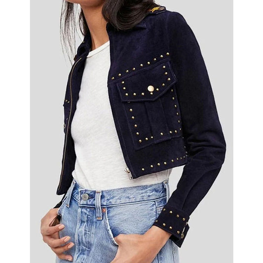 A cropped navy blue suede jacket with gold-tone metal studs, worn by a model over a white t-shirt and light-wash blue jeans against a light gray background.