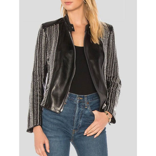 A woman wearing a black moto-style jacket with silver rhinestone-embellished sleeves and shoulder panels, styled with a black top and blue jeans against a light gray background.
