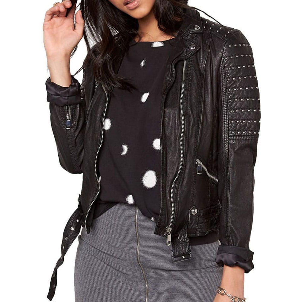 A woman wearing a black faux-leather moto jacket with silver studs and zippers, styled over a black and white polka dot top and a gray skirt, against a plain white background.