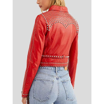 A woman shown from the back wearing a cropped red leather jacket heavily decorated with silver studs, paired with light blue jeans, against a solid gray background.