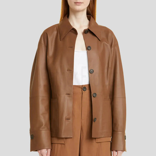 A woman wearing a brown faux-leather jacket over a white top and matching brown trousers, shown from the neck down against a solid gray background.