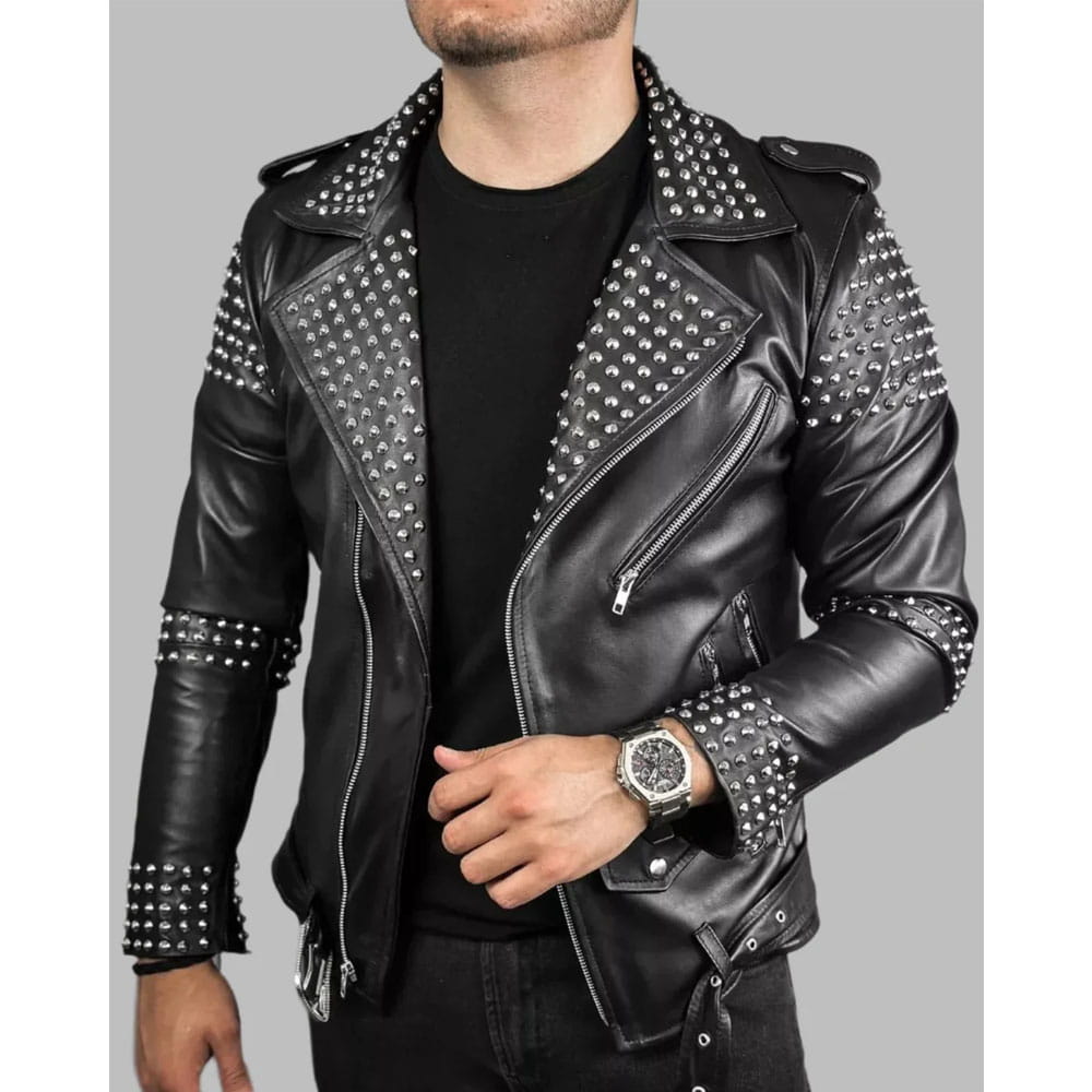 A man wearing a black faux leather moto jacket with silver studs on the shoulders, collar, and front panels, layered over a black t-shirt and black jeans.