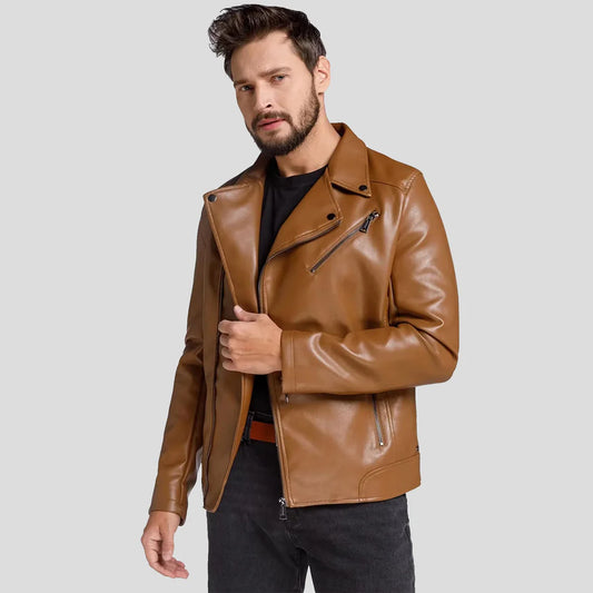 A man wearing a tan brown faux leather motorcycle jacket over a black t-shirt and dark jeans, posing against a solid light gray background.