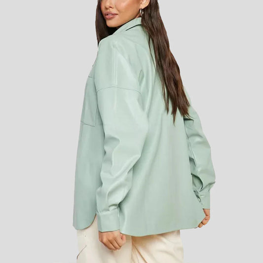 A woman wearing an oversized sage green faux-leather button-up shirt, shown from a three-quarters back view against a solid light gray background.