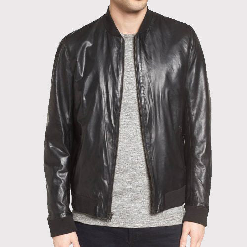 A man wearing a black leather bomber jacket over a gray heathered crewneck sweater, shown from the chin down against a light gray background.