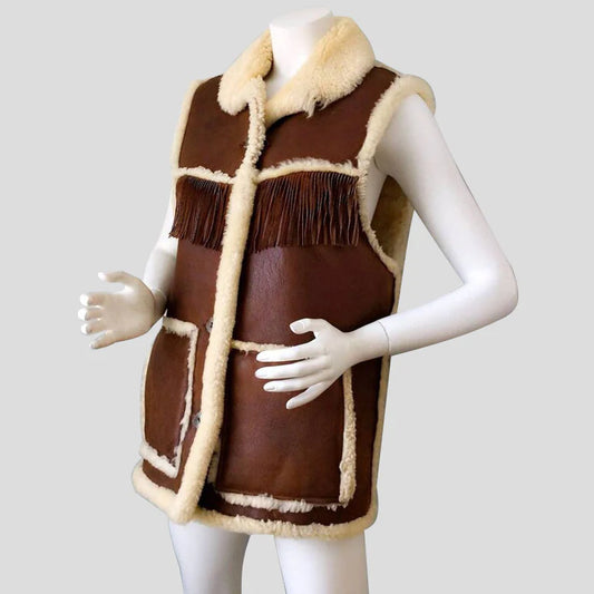 A brown faux-shearling sleeveless vest with cream-colored faux fur trim and fringe details, displayed on a white mannequin against a light gray background.