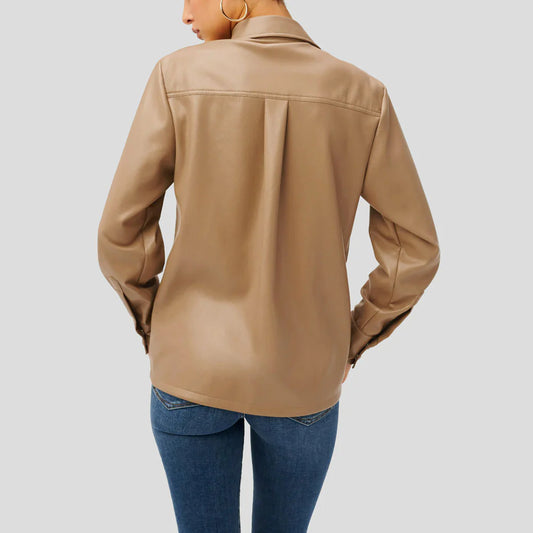 A woman shown from the back wearing a tan faux-leather button-up shirt and blue jeans against a solid gray background.