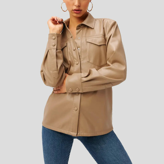 A woman wearing a beige long-sleeve button-up shirt with chest flap pockets and blue jeans, shown from the mouth down against a light gray studio background.